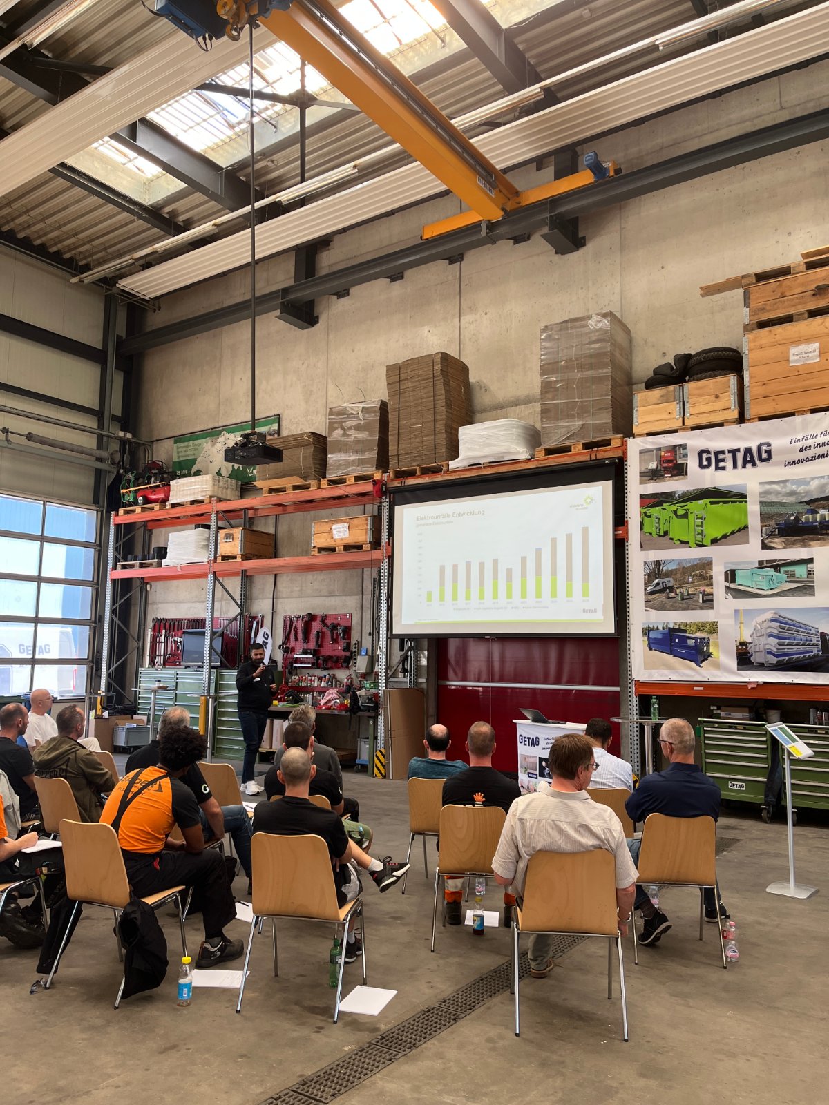 Teilnehmende des GETAG-Workshops sitzen bei einer Präsentation und einem Fachvortrag zur Arbeitssicherheit in der Halle.