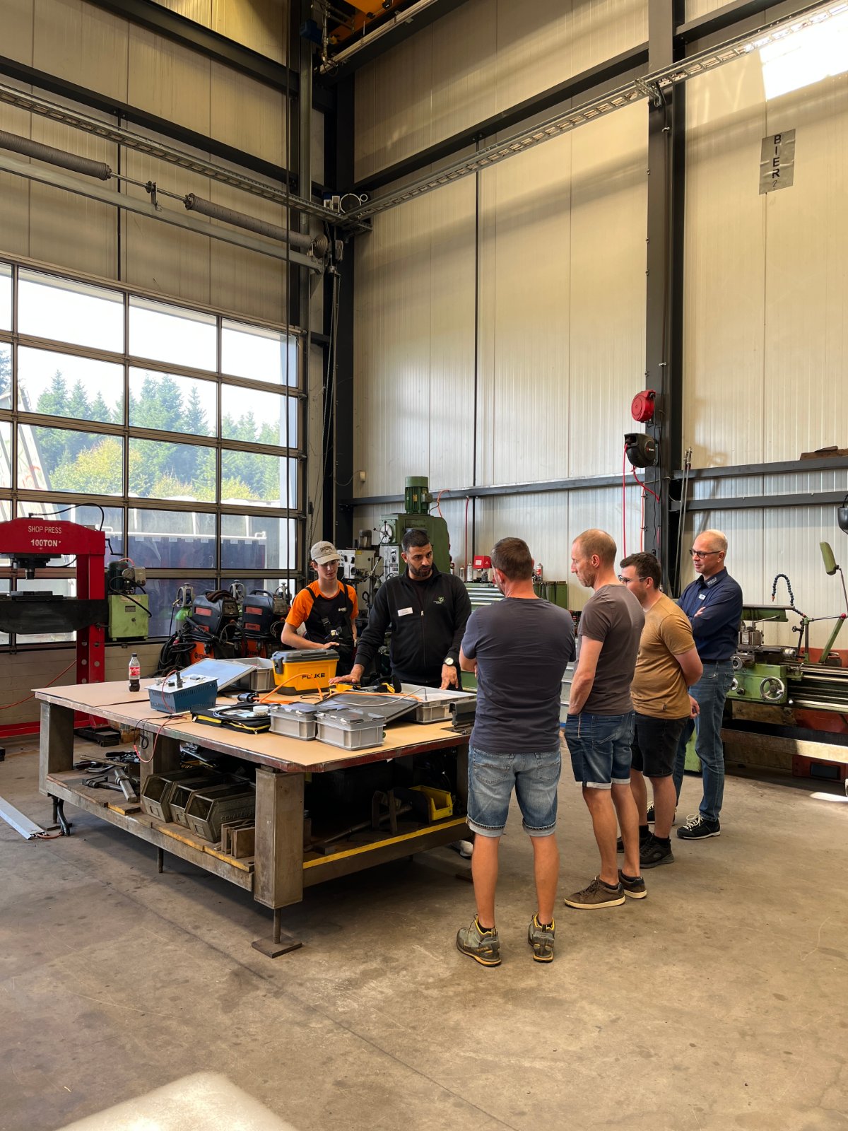 Teilnehmende und Kursleiter des GETAG-Workshops während der Praxiseinheit in der Werkstatthalle an einer Werkbank.
